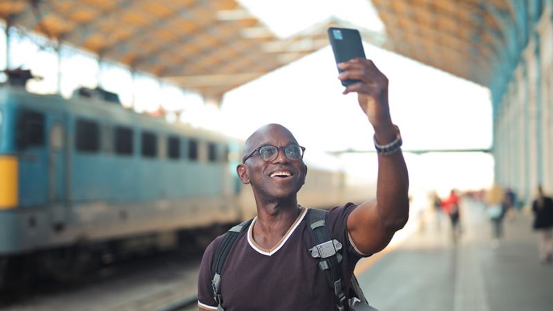 A man at a train station holding his phone in the air