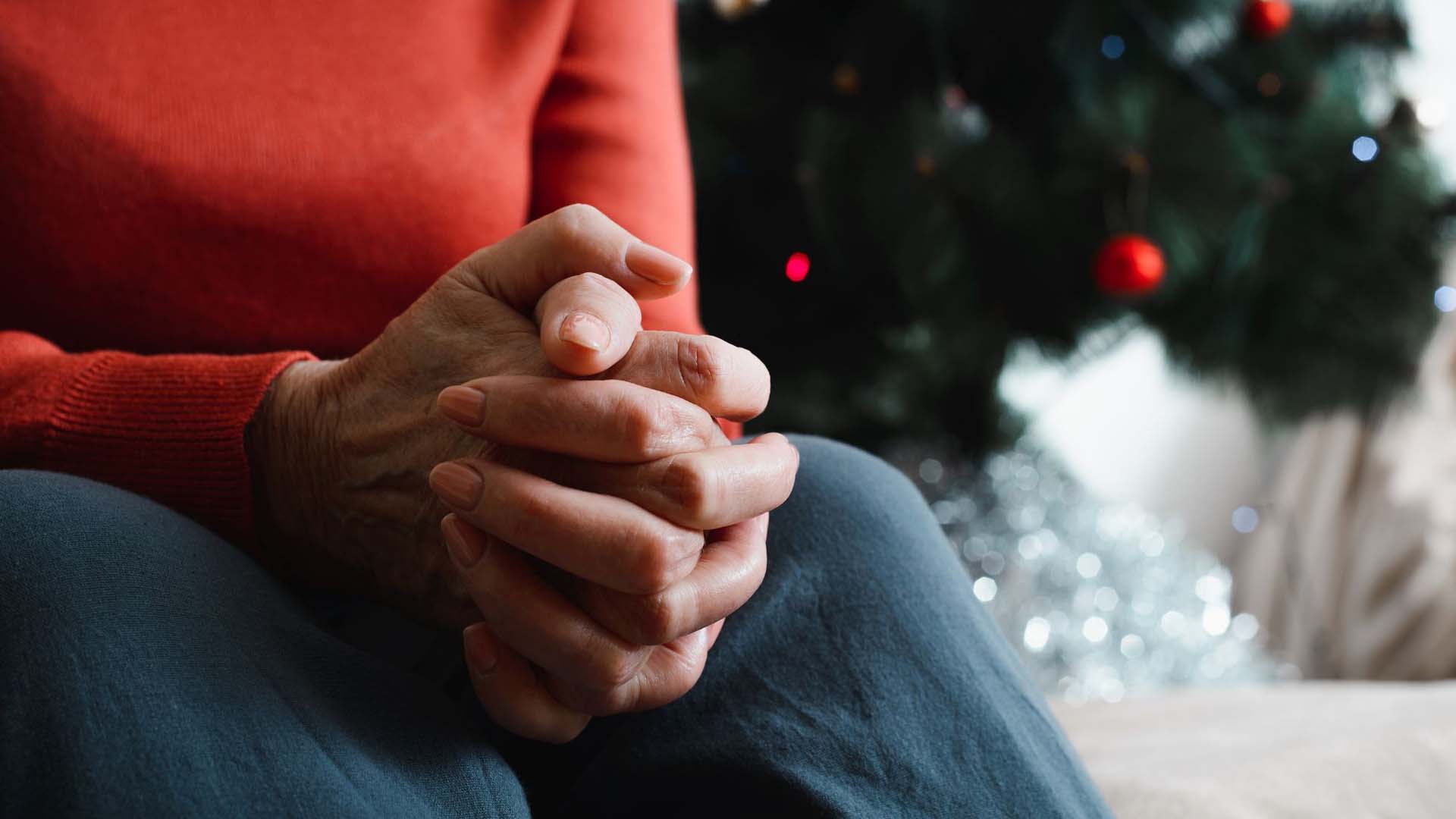 woman sitting next to a christmas tree with hands clasped