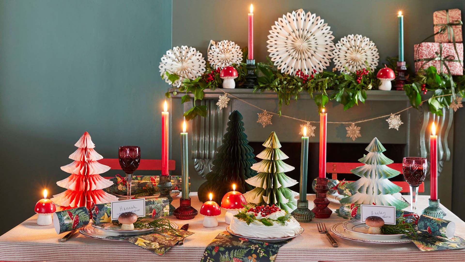 A dining table dressed for Christmas with paper tree decorations, candles and Christmas crackers