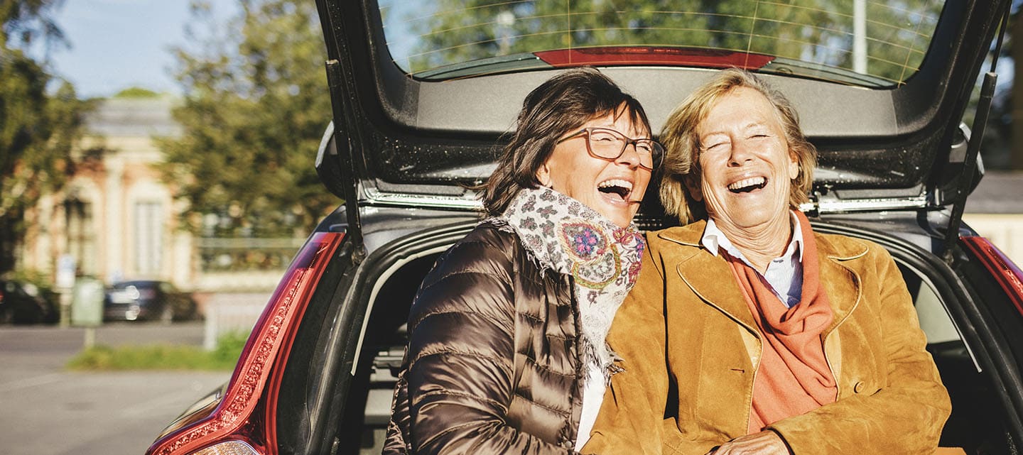 Two ladies sitting on the edge of a car boot laughing