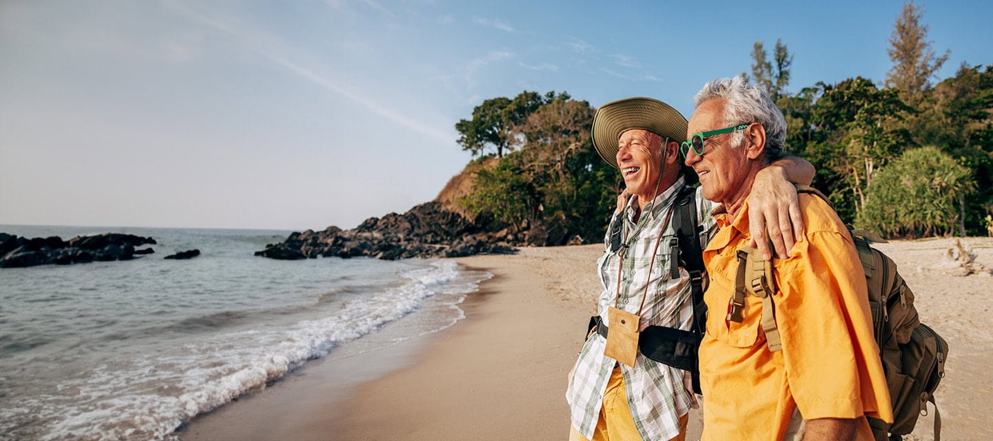 Happy senior couple standing with arms around and looking at sea on beach 