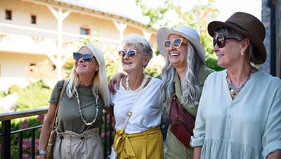 Group of senior female friends standing outdoors on hotel terrace arriving for summer holiday.