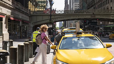 Woman hailing a yellow taxi on a busy street by Grand Central Terminal with American flags in the background