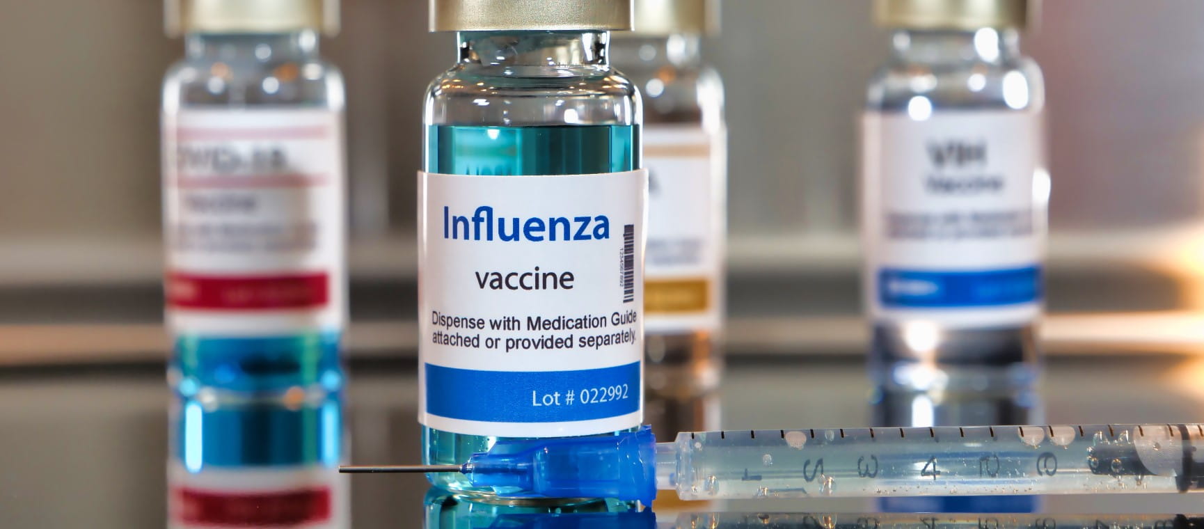 Vials of influenza vaccine bottles with a syringe on black table and stainless steel background | Getty/Bernard Chantal