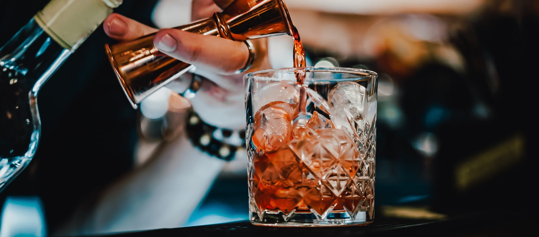 Bartender pouring a shot of vermouth into a crystal tumbler