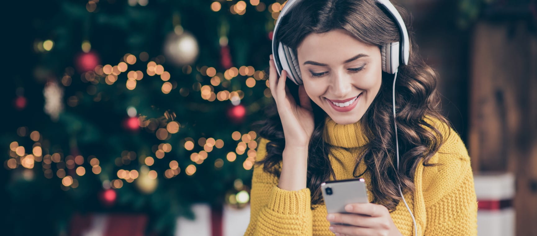 A woman listens to music through headphones in front of her christmas tree