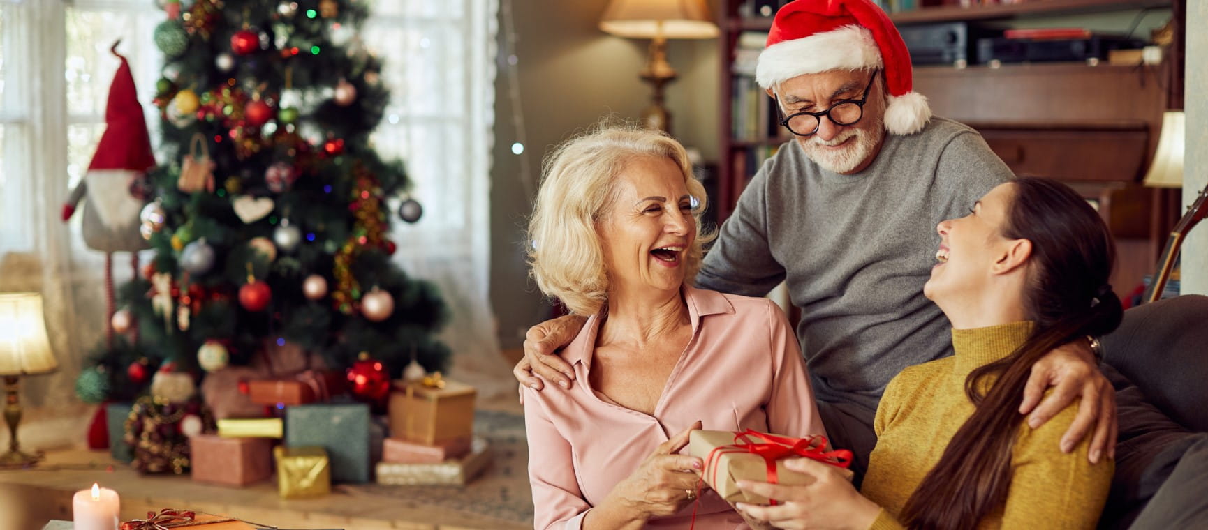 Young woman having fun while receiving Christmas present from her senior parents at home.