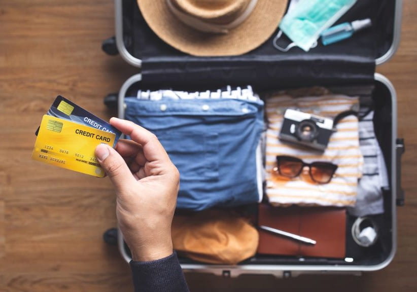 Open packed suitcase with person holding two credit cards