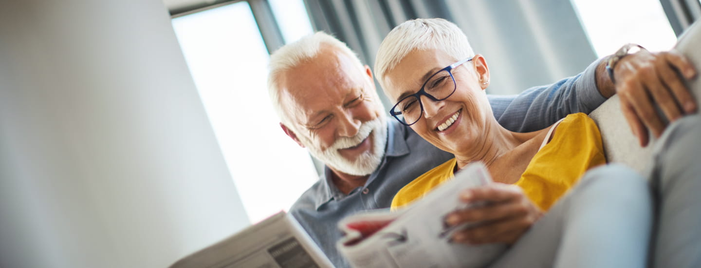 Two smiling older people sitting on a sofa looking the Saga Equity Release guide