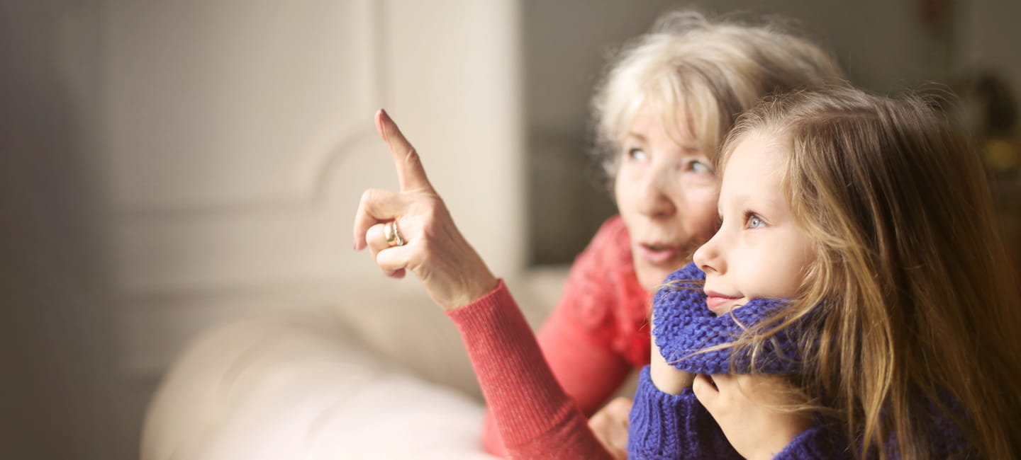 A grandparent with grandchild pointing and looking at something that's out of the image