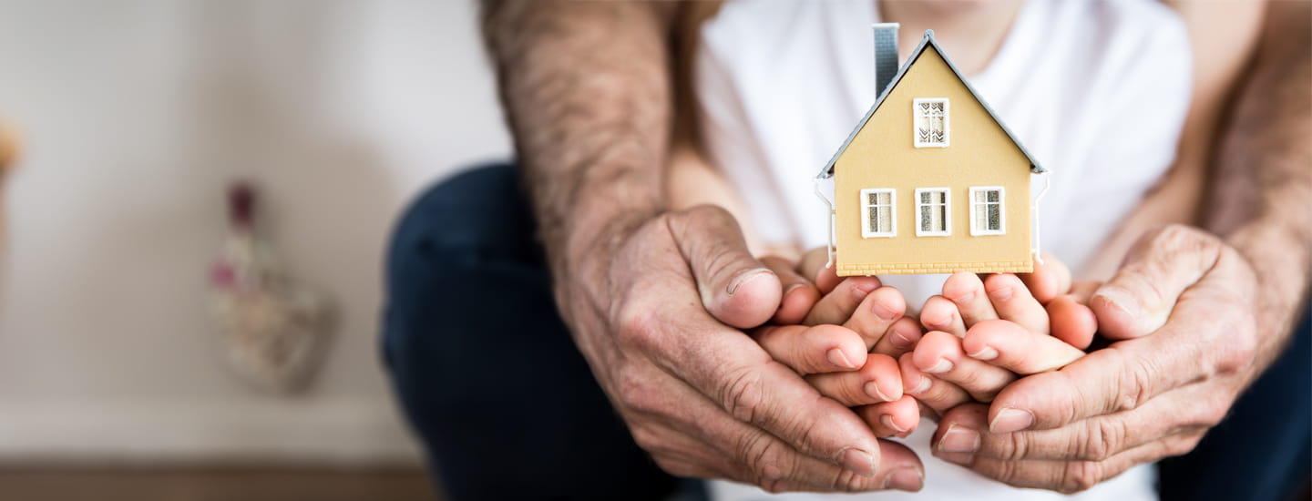 An adult and child's hands cupped together holding a small wooden house