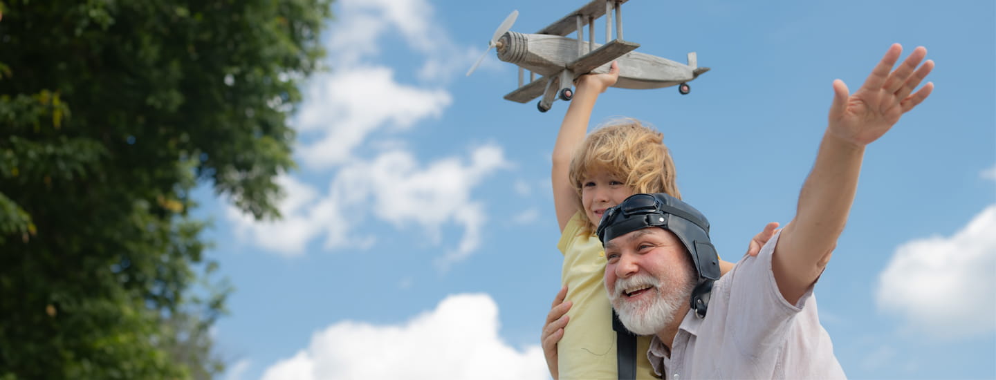 A grandfather carrying his grandson in the air as they play with a toy airplane