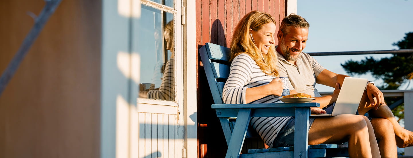 Two people sitting on a bench looking at a laptop and laughing