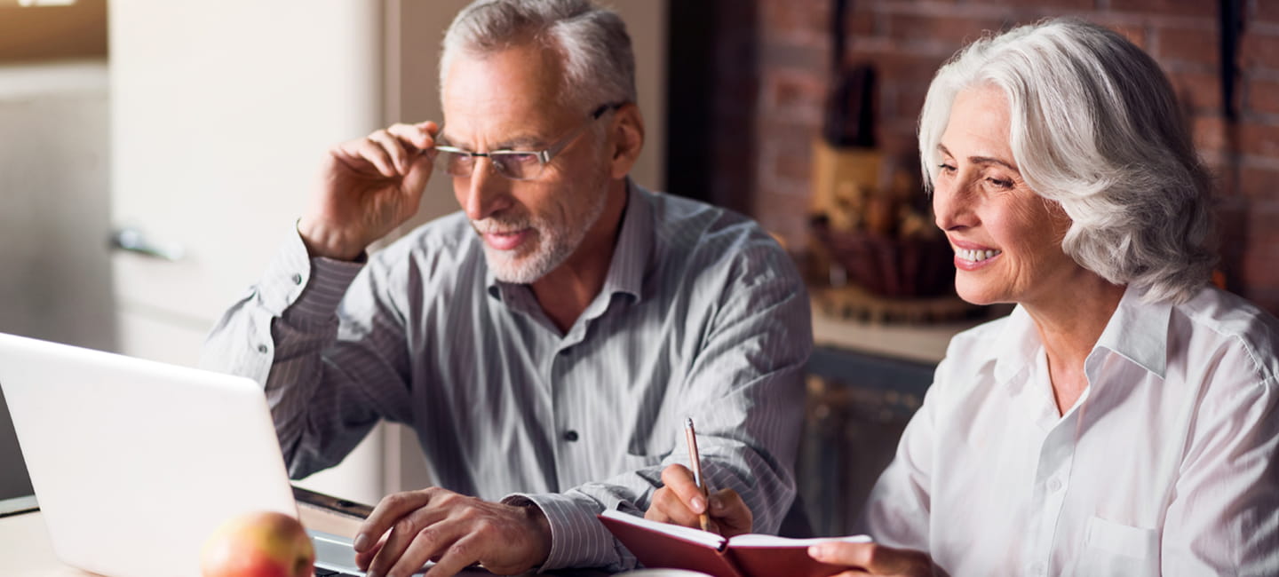 Two older people looking at a laptop and taking notes