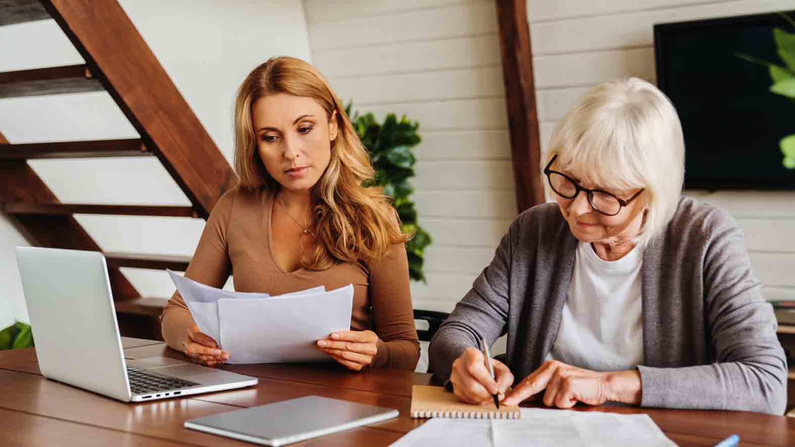 An older woman with help of her daughter completing paperwork at home