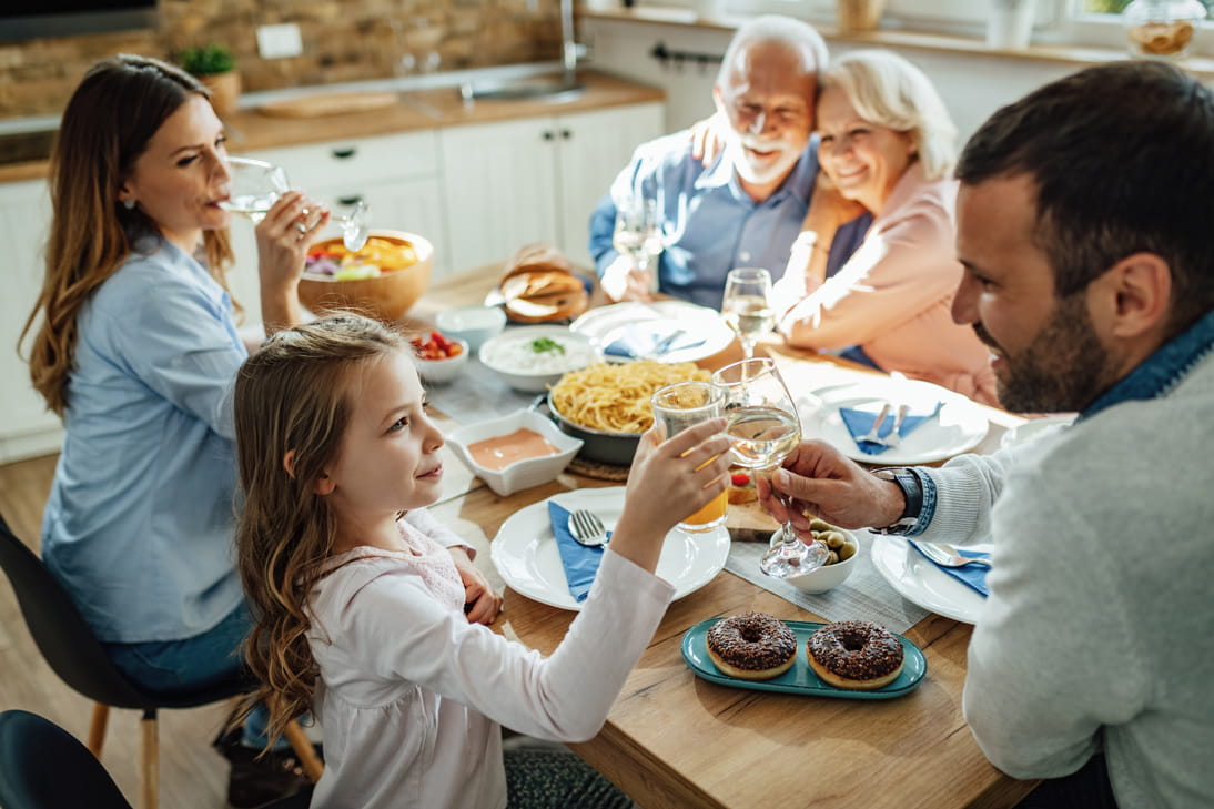 A family including grandparents sat having a meal smiling and happy