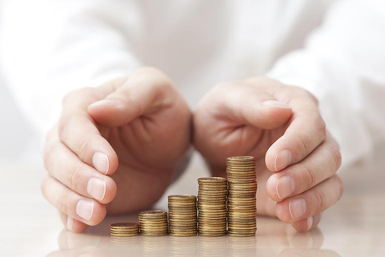 Two hands held protectively around 5 stacks of coins